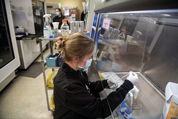 A woman wearing a white mask in a laboratory, holding a test tube